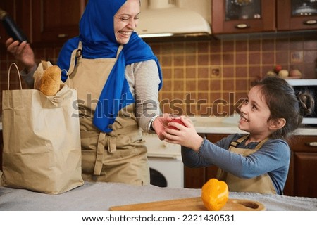 Selective focus. Happy Middle-Eastern family of Muslim woman, loving happy mother in blue hijab and her adorable little daughter, having fun together while unpacking grocery bag in the kitchen at home Royalty-Free Stock Photo #2221430531