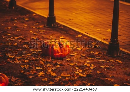 Scary Jack O Lantern halloween pumpkins in darkness on ground among dry leaves at street. Hallows eve decoration funny glow pumpkin with candles on dark background in open air near house