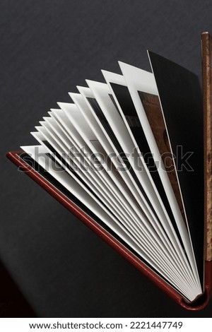 A stylish open-page photo book with a leather cover in burgundy and brown colors, hardcover, stands on a gray tabletop indoors.