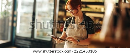 Happy supermarket owner using a digital tablet while standing in her grocery store. Successful entrepreneur running her small business using wireless technology. Royalty-Free Stock Photo #2221453105