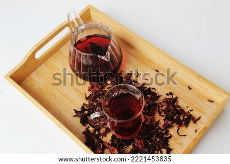 Pomegranate flowers tea is brewed in glass teapot and poured into a cup on a bamboo tray. Beautiful ruby infusion. White background. Flower drink, healthy food concept
