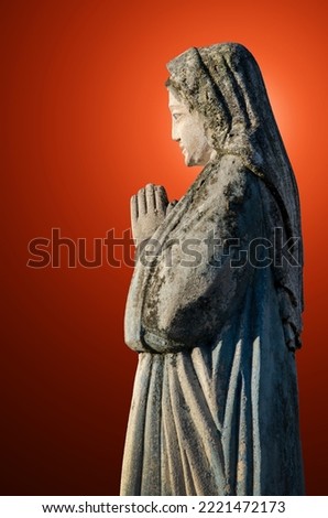 An ancient sculpture of the Virgin Mary with folded hands in prayer against the background of rays of light, which symbolize the personification of the Holy Spirit.
