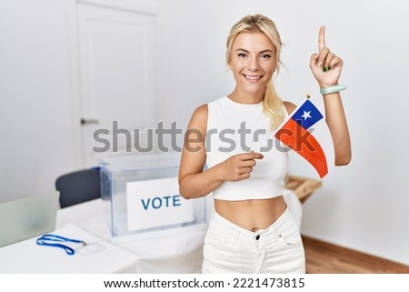 Young caucasian woman at political campaign election holding chile flag smiling with an idea or question pointing finger with happy face, number one 