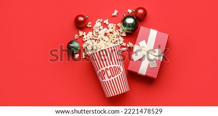 Bucket of tasty popcorn with Christmas balls and gift on red background