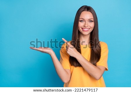 Portrait of good mood nice girl straight hairdo yellow t-shirt indicating empty space presenting product isolated on blue color background
