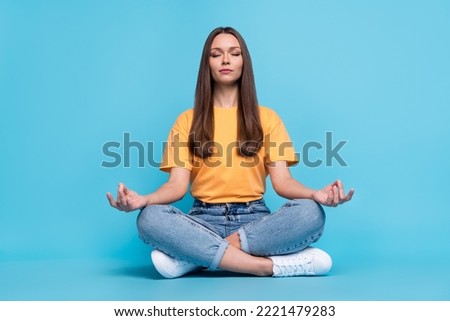 Photo of dreamy adorable young lady wear yellow t-shirt sitting legs crossed practicing yoga isolated blue color background