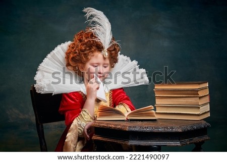 Portrait of little red-headed girl, child in costume of royal person reading book isolated on dark green background. Concept of historical remake, comparison of eras, medieval fashion, emotions, queen Royalty-Free Stock Photo #2221490097