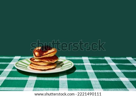 Plate of delicious sweet pancakes with jam on green tablecloth over green background. Vintage, retro style interior. Food pop art photography. Complementary colors. Copy space for ad, text