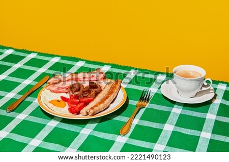 Plate of English breakfast with fried eggs, bacon, sausage, mushrooms and tomato on green tablecloth with coffee. Vintage, retro. Food pop art photo. Complementary colors. Copy space for ad, text