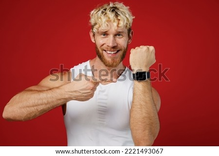 Young fun strong sporty toned sportsman man wear white clothes spend time in home gym use point finger on smart watch with blank screen isolated on plain red background. Workout sport fit body concept Royalty-Free Stock Photo #2221493067
