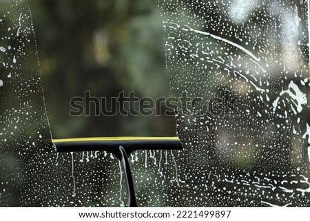 Cleaning foam from glass with squeegee indoors, closeup