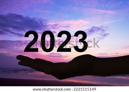 Hand offering 2023 numbers, sunset background, new year card
