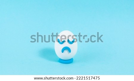Lonely egg with a sad expression close up. The concept of a pessimistic outlook on life. Blue background. Сopy space. Close up. Royalty-Free Stock Photo #2221517475