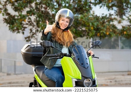 Red-haired woman riding a motorcycle on a city street with thumbs up sign Royalty-Free Stock Photo #2221525075