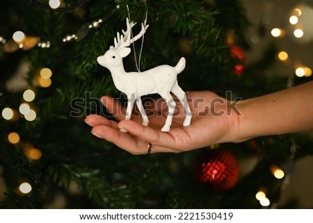 New Year and Christmas greeting card with a deer. A hand holds a deer toy near the Christmas tree.
