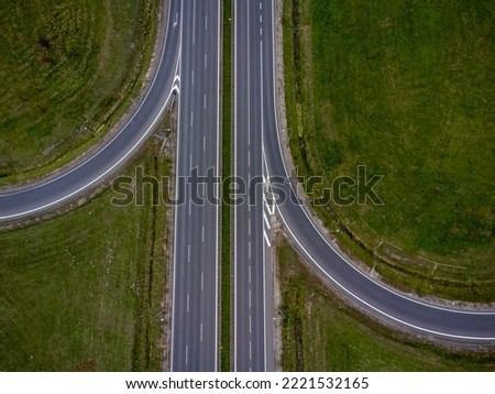 The picture presents intersection of roads visible from above with multiple cars and grass around. 