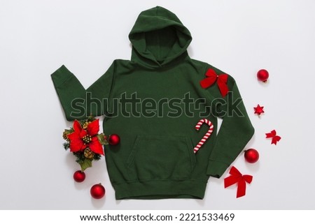 Close up green blank template hoodie copy space. Christmas Holiday concept. Top view mockup hoodie. Red holidays decorations on jumper white background. Happy New Year accessories. Selective focus