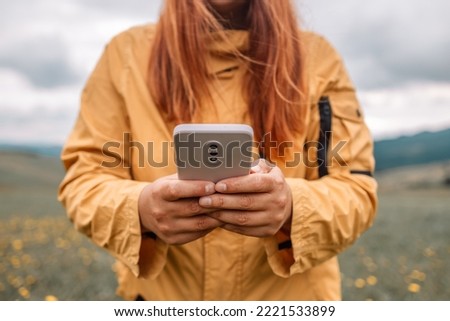 Young woman relaxing on the top mountains. Girl traveler hiker holds a mobile phone in her hands and takes pictures of the landscape. Side view.