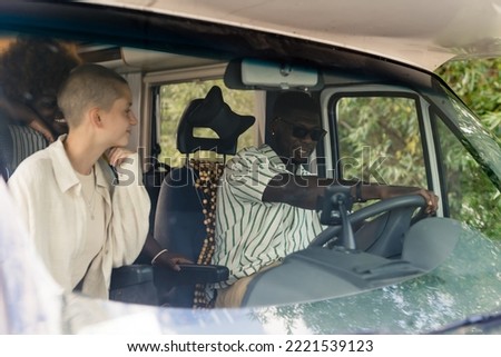 Multi-ethnic group of close friends having a summer road trip in a camping van, driving, talking and laughing heartily inside their vehicle. Front seats close-up. High quality photo