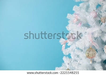 Christmas card with white christmas tree with beautiful decorations and toys. Artificial tree on blue background with copy space, place for text. Happy new year, holiday symbol, winter miracle.