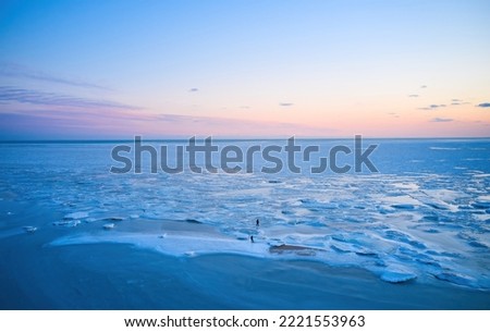 Aerial view - two people walk on ice on sunset over the frozen sea. Winter landscape on seashore during dusk. View from above of melting ice in ocean on sunrise. Global warming. Vivid colorful skyline Royalty-Free Stock Photo #2221553963