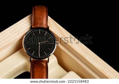 Luxury gold watch with black dial and light brown strap. Watch on a beautiful wooden case holder, on a black background. Womenmen fashion