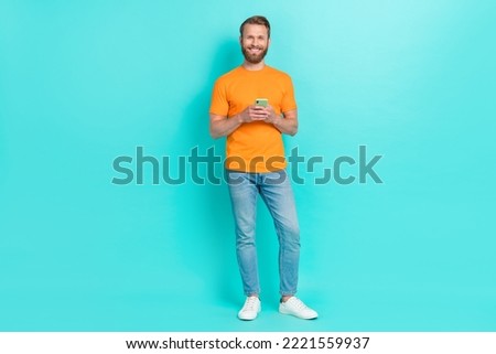 Full size photo of boyfriend guy hold telephone wear orange t-shirt jeans sneakers isolated on teal color backgroiund