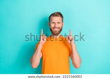 Photo of toothy beaming optimistic man with blond hairstyle dressed orange t-shirt directing empty space isolated on teal color background