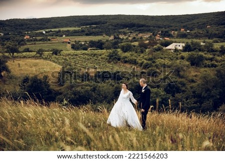 The bride and groom hold hands and look to the future in the middle of nature, the newlyweds walk together,wedding photography,until death do us part