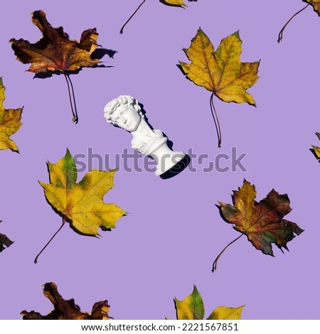 Male plaster bust, popular souvenir and dry colorful leaves, creative autumnal pattern on a pastel purple background. 