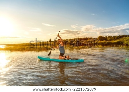 A man in shorts on a SUP board with a paddle floats on the water in the rays of the setting sun. Horizontal photo