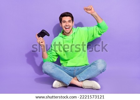 Full length photo of excited lucky man wear green hoodie rising fist playstation isolated purple color background