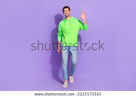 Full length photo of funny cheerful man wear green hoodie walking waving arm isolated purple color background Royalty-Free Stock Photo #2221573165