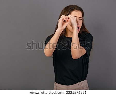 Happy excited woman doing spyglass sign looking in by fingers the hands with surprising opened mouth in black t-shirt. Concept studio portrait