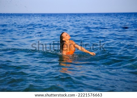 A young brunette woman in an orange bathing suit is swimming in the sea. Beach vacation girl on a sunny day