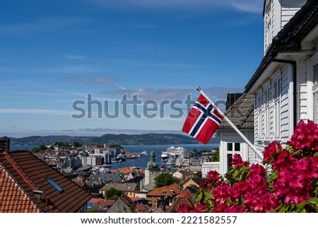 The Norwegian flag is placed on the facade of the house in Bergen, behind the flag you can see the city of Bergen with the fjord Royalty-Free Stock Photo #2221582557