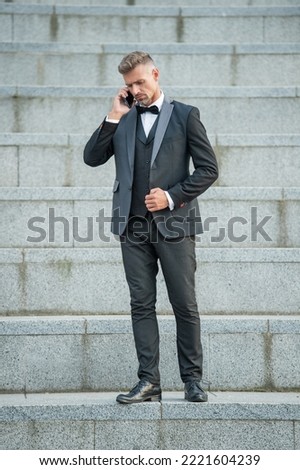 grizzled man in bowtie suit outdoor. businessman man using phone. man boss talking on smartphone Royalty-Free Stock Photo #2221604239