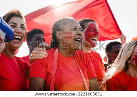 Multiracial red sport football fans celebrating team victory in championship game at stadium - Soccer supporters having fun in crowd - Focus on African senior woman face Royalty-Free Stock Photo #2221605851