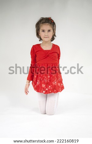 Beautiful little girl dressed in red playing and posing with light grey background 
