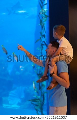 Dad and son spend time together in the Aquarium. Son sits on dad's back and explores the underwater world Royalty-Free Stock Photo #2221611037