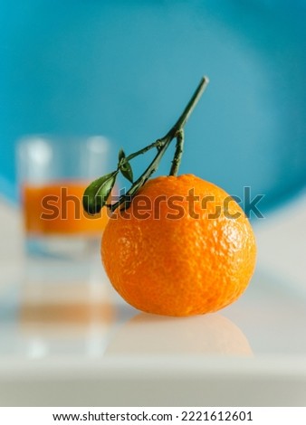 Orange mandarin on white table, cyan background and blurred glass behind