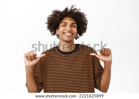 Confident guy pointing at himself and looks proud, self-promoting, feeling high self-esteem, stands over white studio background