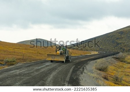 Grader road maintenance heavy equipment on gravel dirt road of remote Dempster Highway in arctic tundra landscape of northern Yukon Territory, YT, Canada Royalty-Free Stock Photo #2221635385