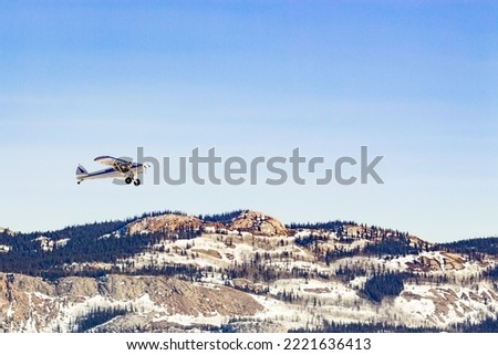 Small bush plane aircraft take-off in Yukon Territory winter landscape of boreal forest taiga rocky hills, YT,  Canada Royalty-Free Stock Photo #2221636413