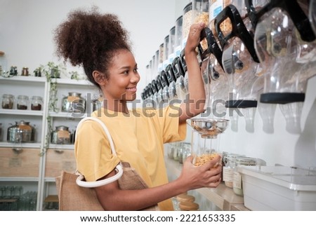 African American female customer fills cereal foods in glass jar, lever the reusable container in a refill store, and zero-waste and plastic-free grocery, environment-friendly, sustainable lifestyles. Royalty-Free Stock Photo #2221653335