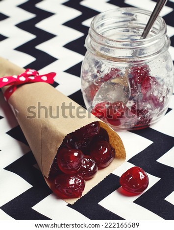 Glace cherries in paper cone vintage jar on chevron background