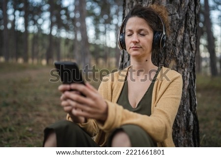 One woman young adult caucasian female sit alone in the park or forest in nature with headphones preparing for guided meditation self-care manifestation practice mental emotional balance concept