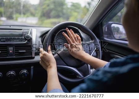 Woman pushing horn while driving sitting of a steering wheel press car, honking sound to warn other people in traffic concept. Royalty-Free Stock Photo #2221670777