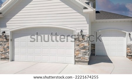 Panorama Puffy clouds at sunset Three car garage exterior with two white garage doors with arched door openings. Garage exterior with white vinyl lap and stone veneer sidings and a view Royalty-Free Stock Photo #2221674255