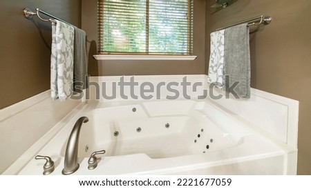 Panorama Alcove bathtub with deck mounted faucet near the window. Bathroom interior with brown walls, flowers on a metal vase at the shelf and two towel bars with hanging towels Royalty-Free Stock Photo #2221677059
